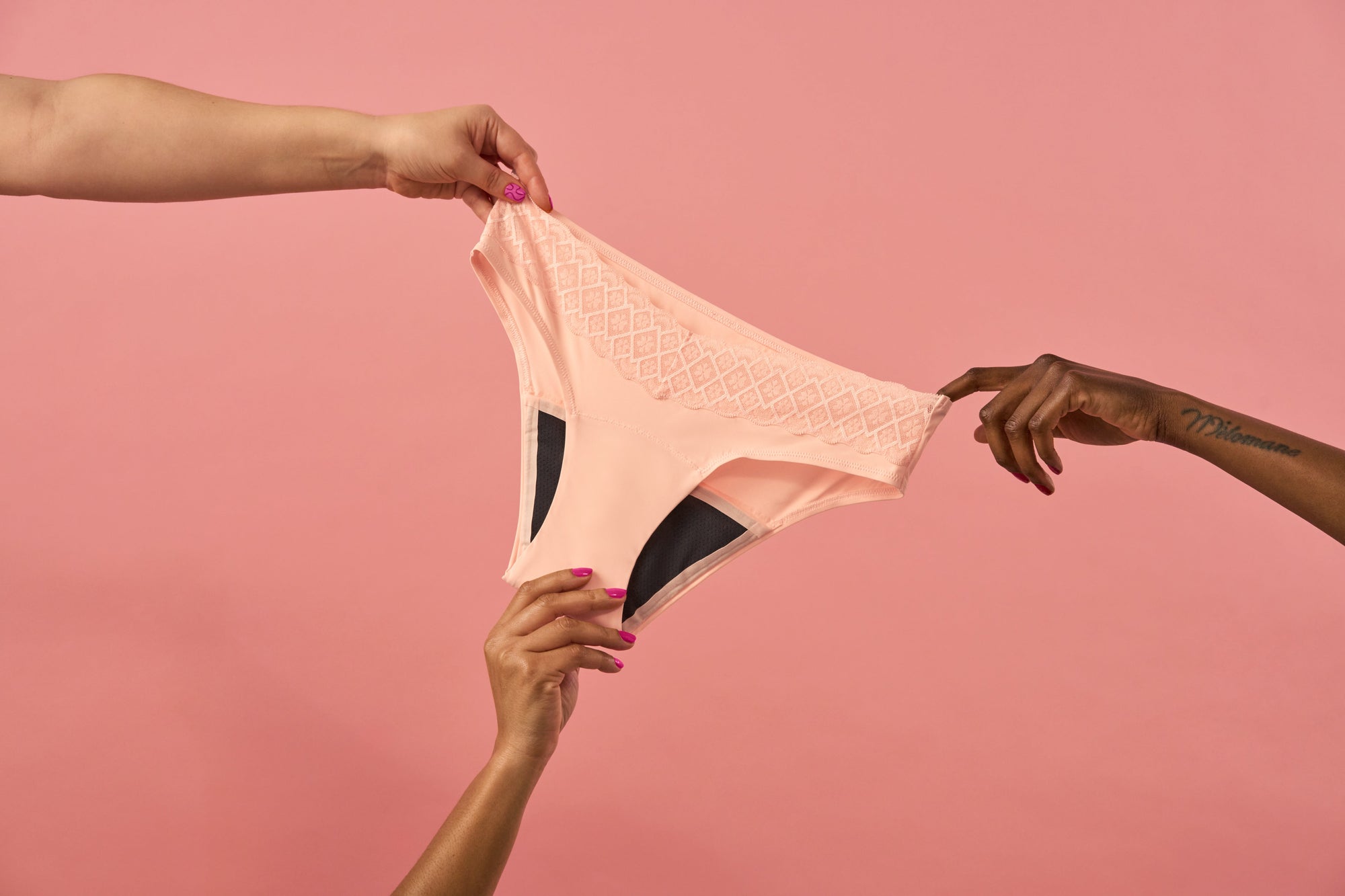 Several hands holding a pair of period pants on a pink background.