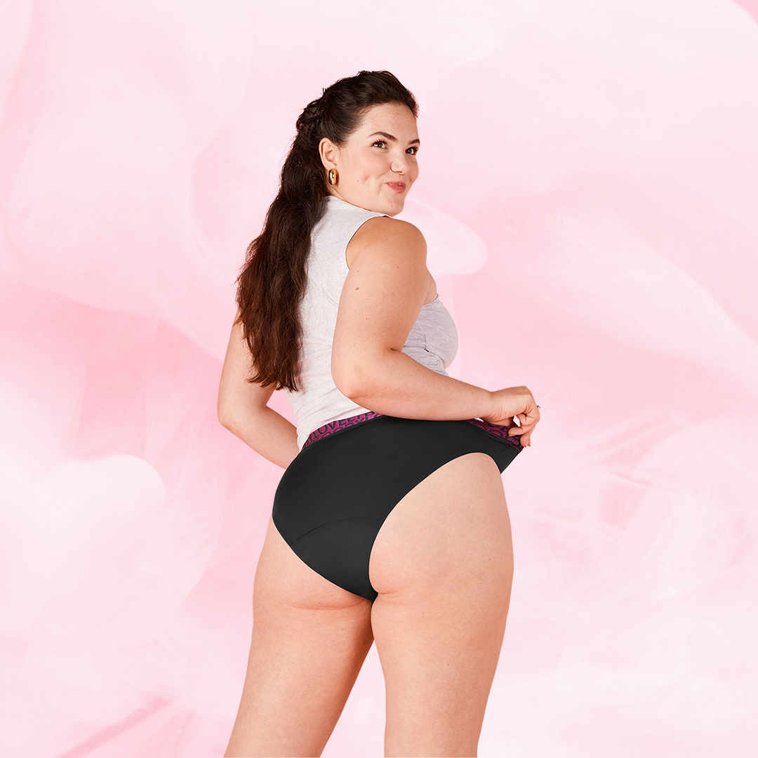 Woman wearing ComfortFit High Leg Moderate period pants, smiling over shoulder.