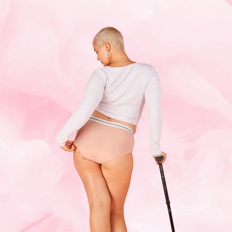 Woman modeling ComfortFit Essentials Hipster Logo Waistband Moderate period pants, showcasing a confident stance with a cane, emphasizing fit and functionality.