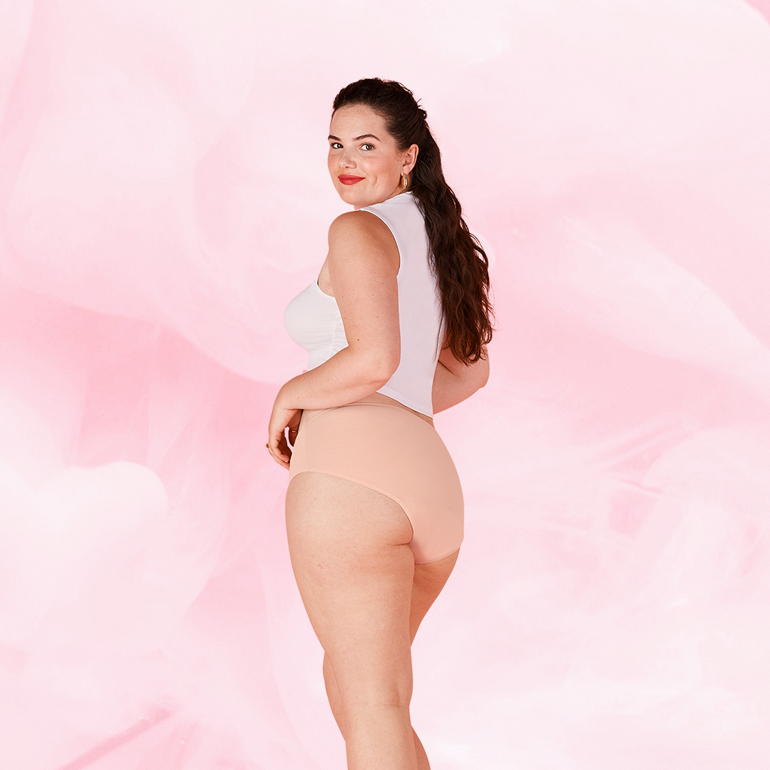ComfortFit Essentials Hipster Moderate features a woman in a white shirt showcasing beige period pants, highlighting their slimline edges and tailored fit for reliable protection.